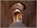 A youngster on a bicyce navigating through narrow mud-brick alley in the old part of Yazd city, Iran.